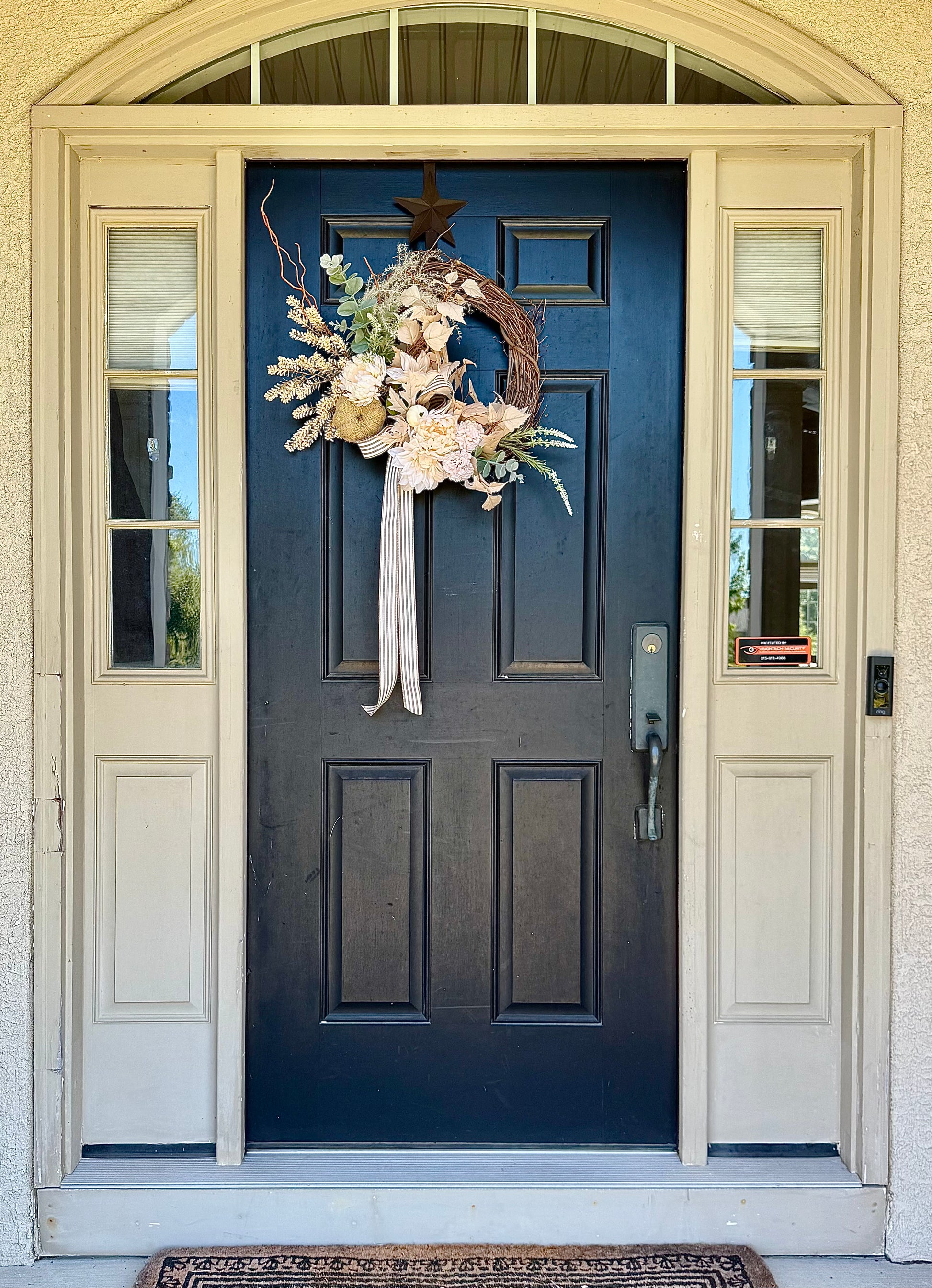 Neutral colored floral wreath on black front door with dried and silk florals and greenery